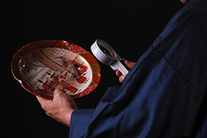 目利きの鑑定士が陶磁器の皿を鑑定している様子